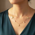 Gold necklace with star, shell, and pearl pendants on a model wearing a green dress.