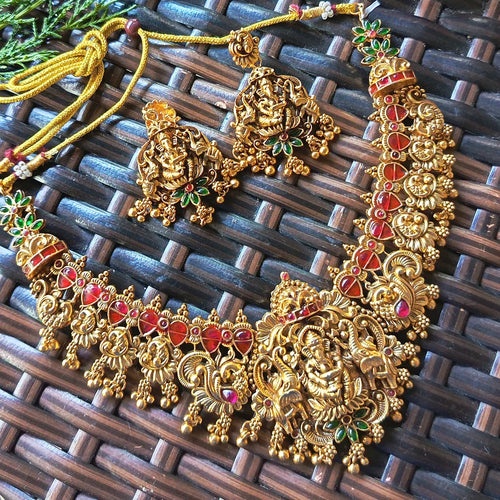 Gold necklace with red and green stones on a woven surface