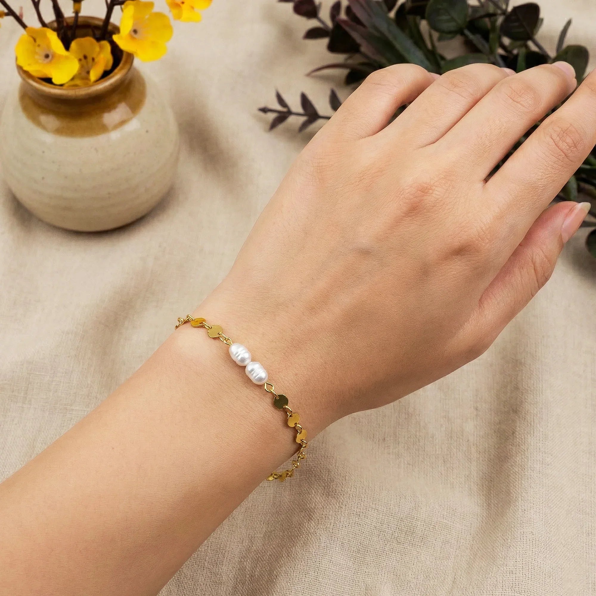 Hand wearing a bracelet with pearls and gold beads on a beige fabric background