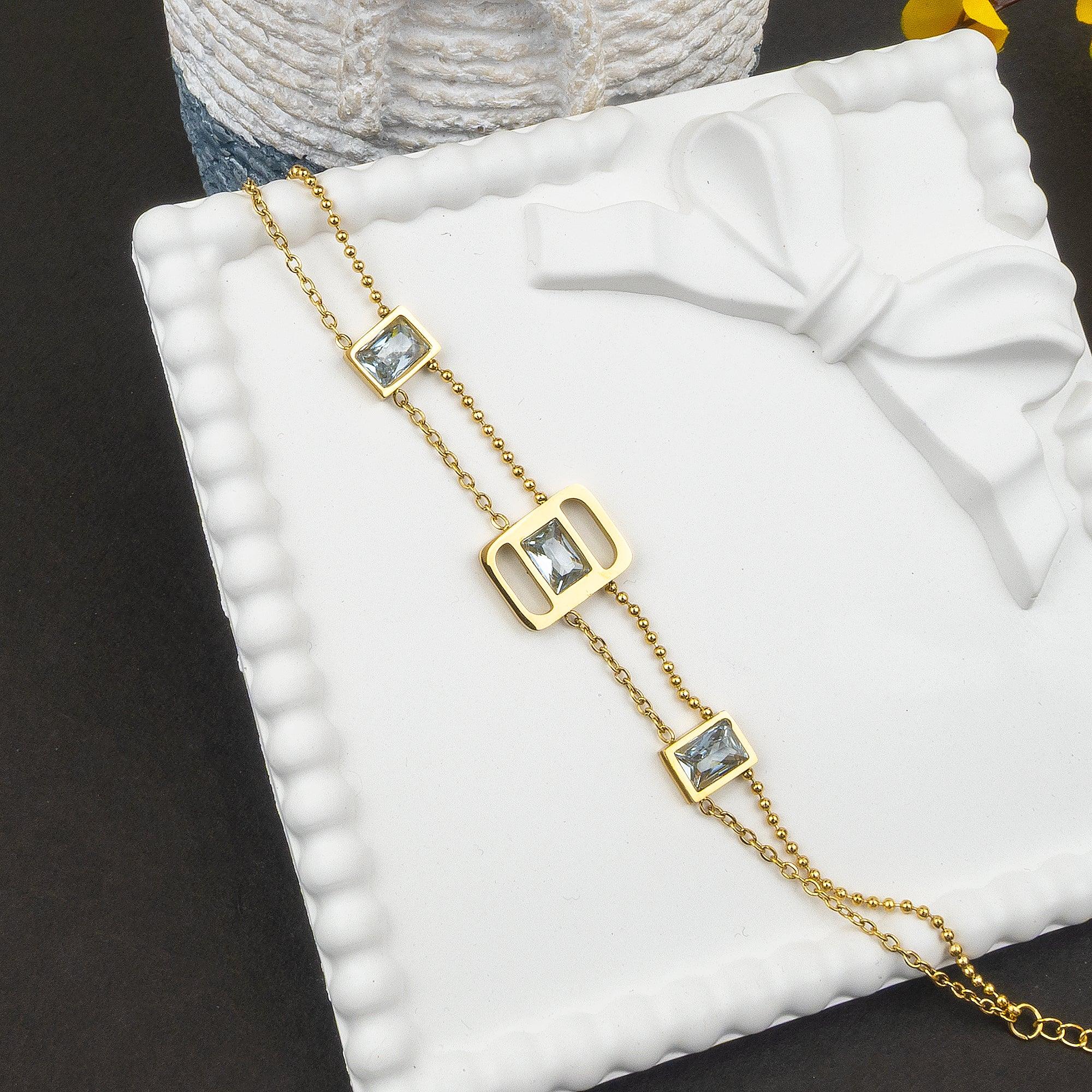 Gold chain necklace with square gemstones on a white cushion
