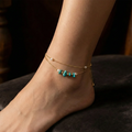 An anklet with turquoise beads on a foot against a dark background