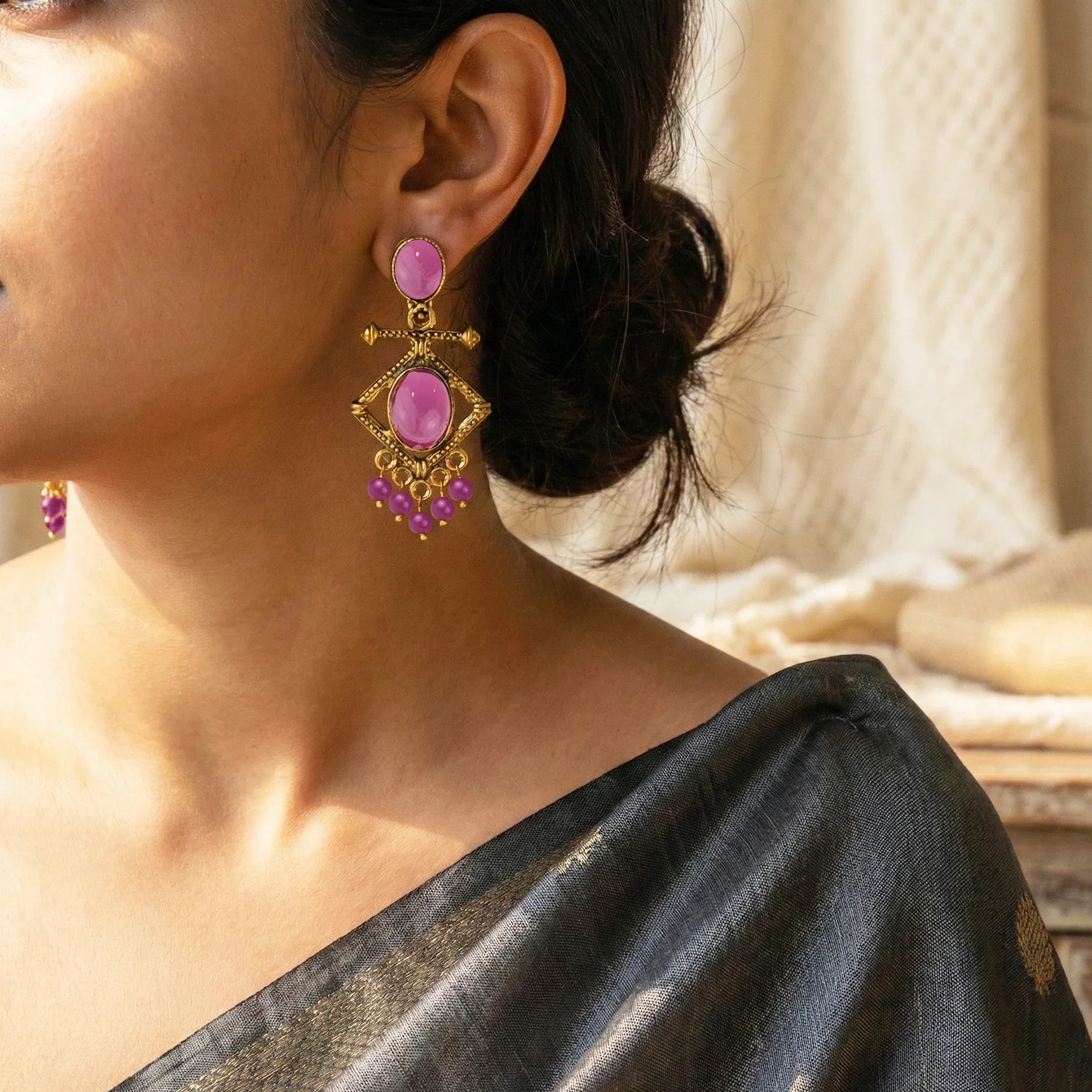 Close-up of a woman wearing pink earrings with gold accents, dressed in a black saree.
