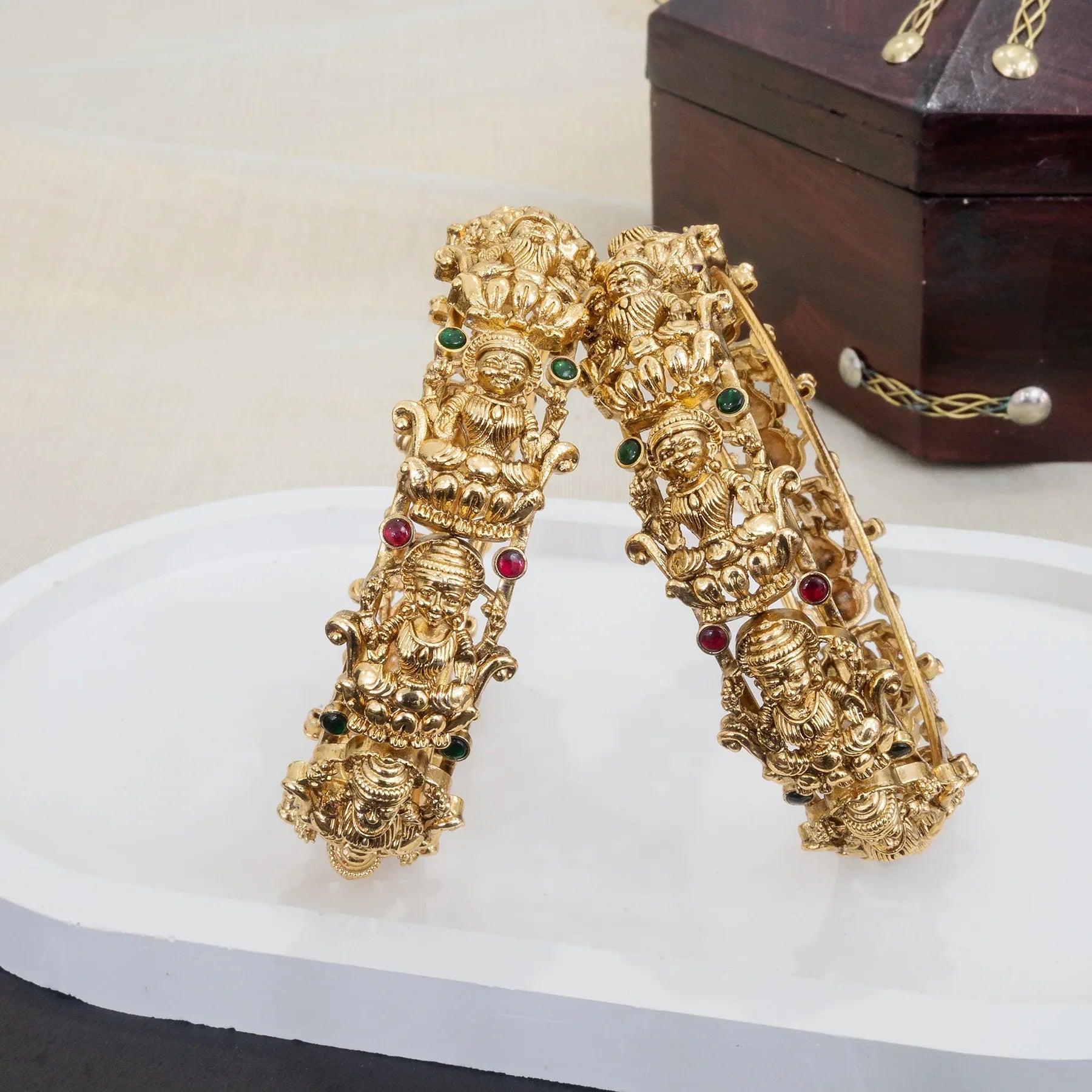 Gold bracelet with intricate designs and gemstones on a white surface.