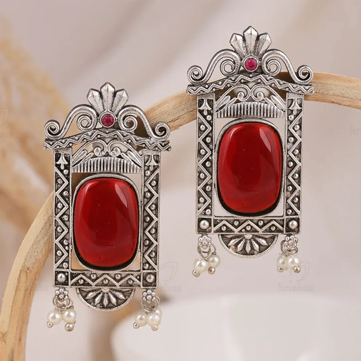 Ornate silver earrings with red stones on a wooden stick