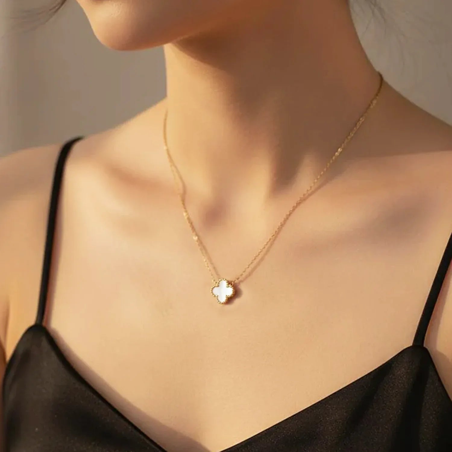 Gold necklace with a clover pendant on a model wearing a black top.