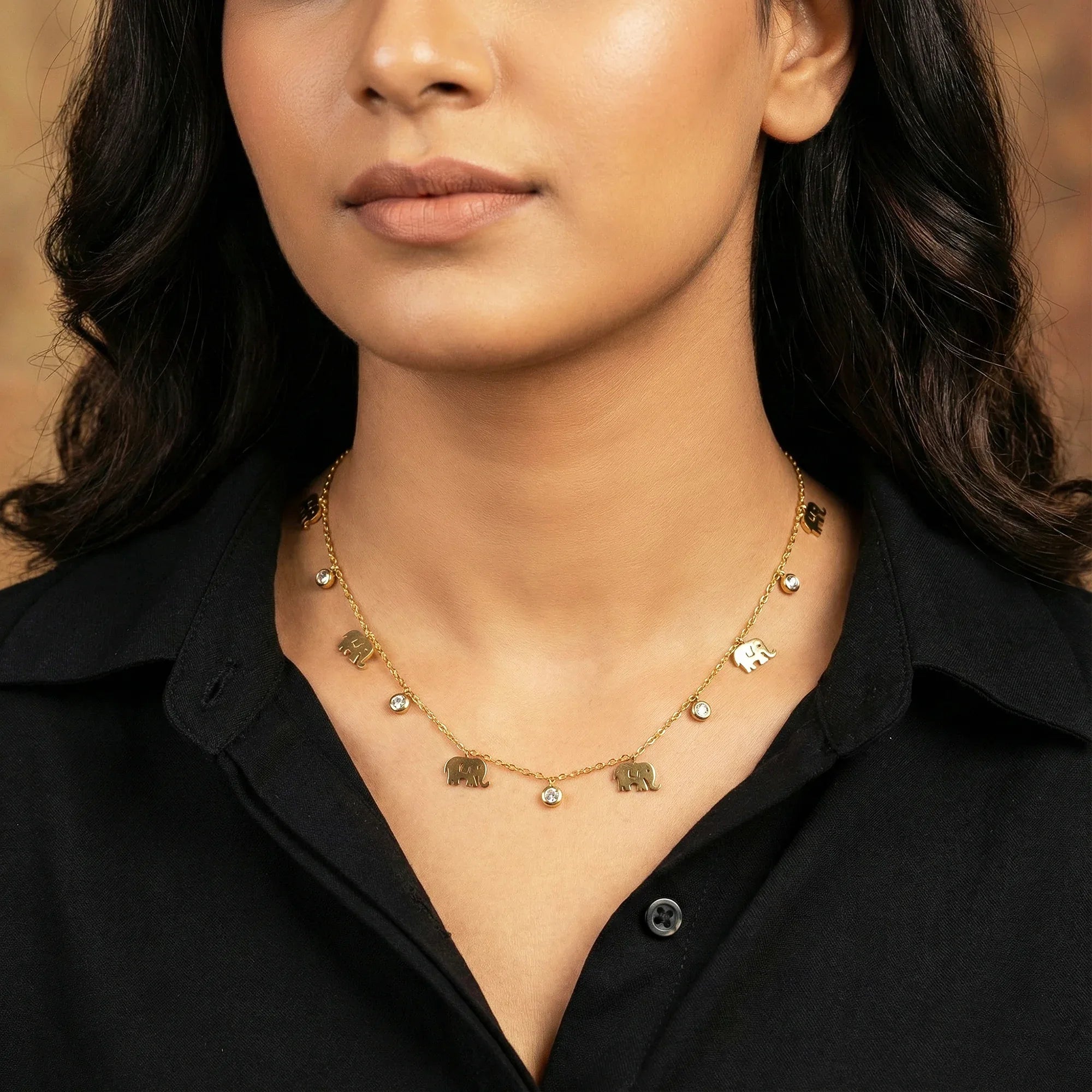 Woman wearing a gold necklace with elephant charms against a neutral background