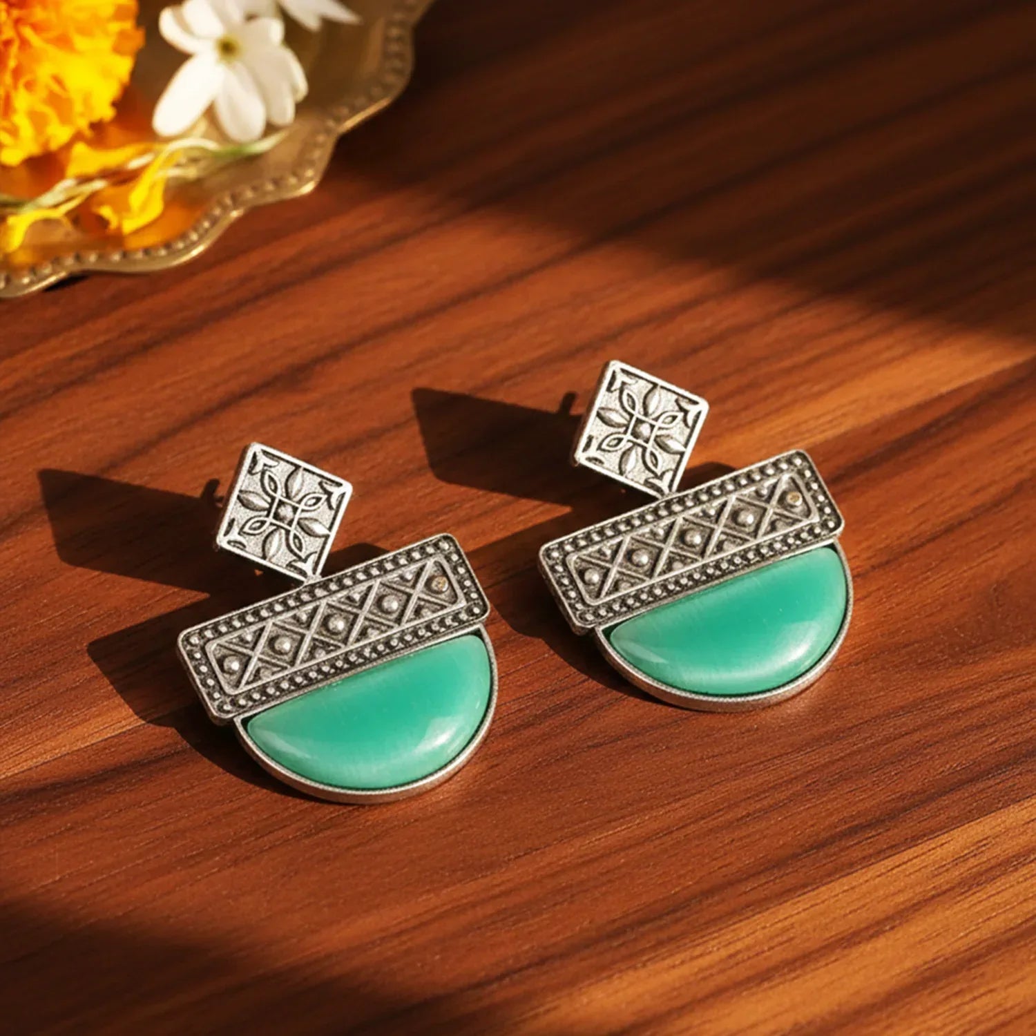 Pair of earrings with turquoise stones and silver patterns on a wooden surface.
