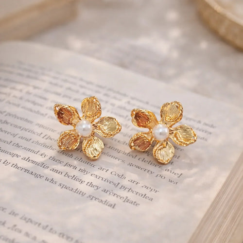 Gold flower-shaped earrings with pearls on an open book