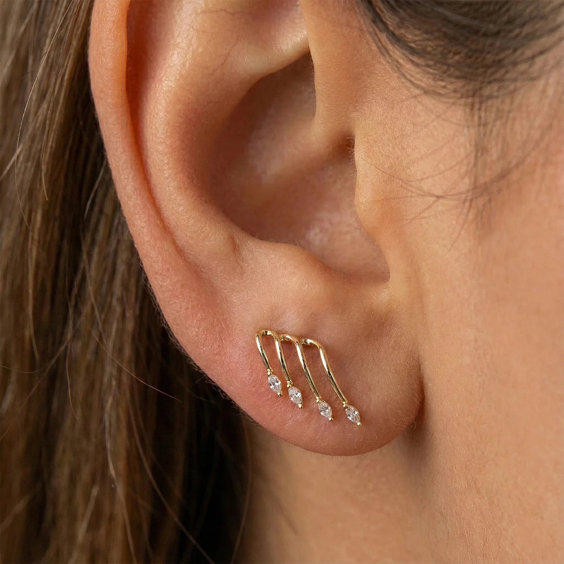 Close-up of an ear wearing a gold earring with three clear gemstones.