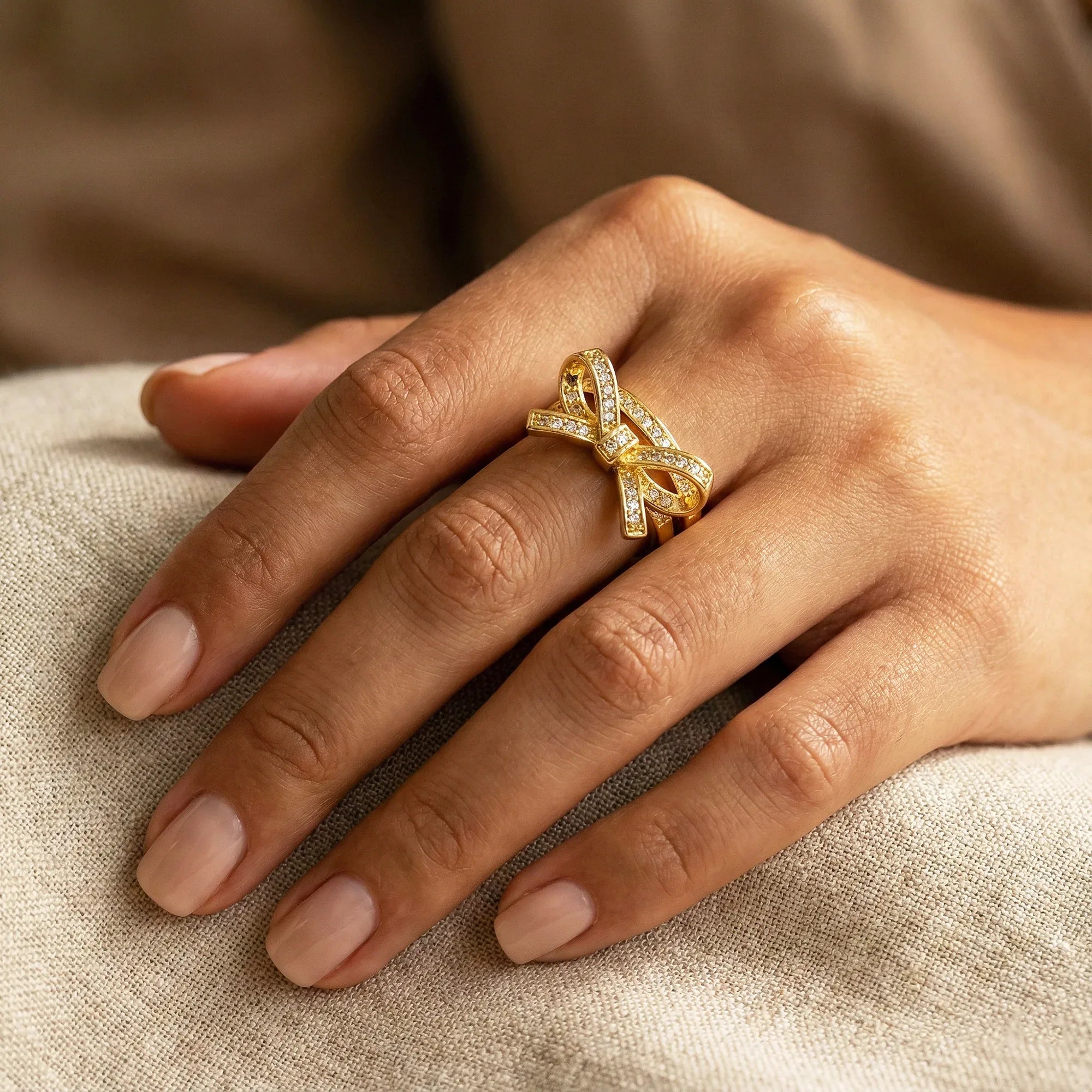 Gold ring with diamonds on a hand resting on beige fabric