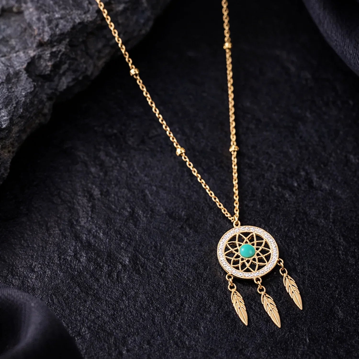 Gold necklace with a dreamcatcher pendant on a dark textured surface