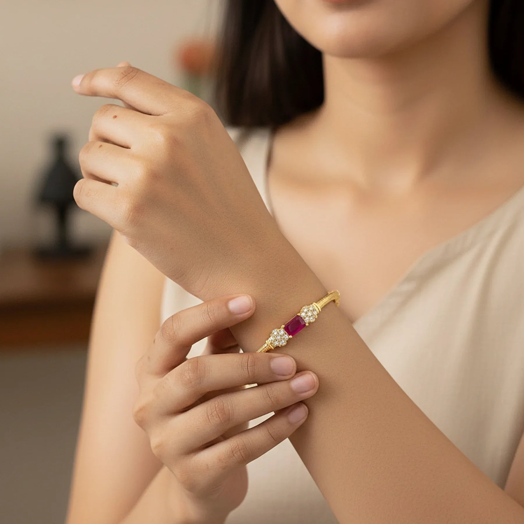 Woman wearing a gold bracelet with red gemstones on her wrist.