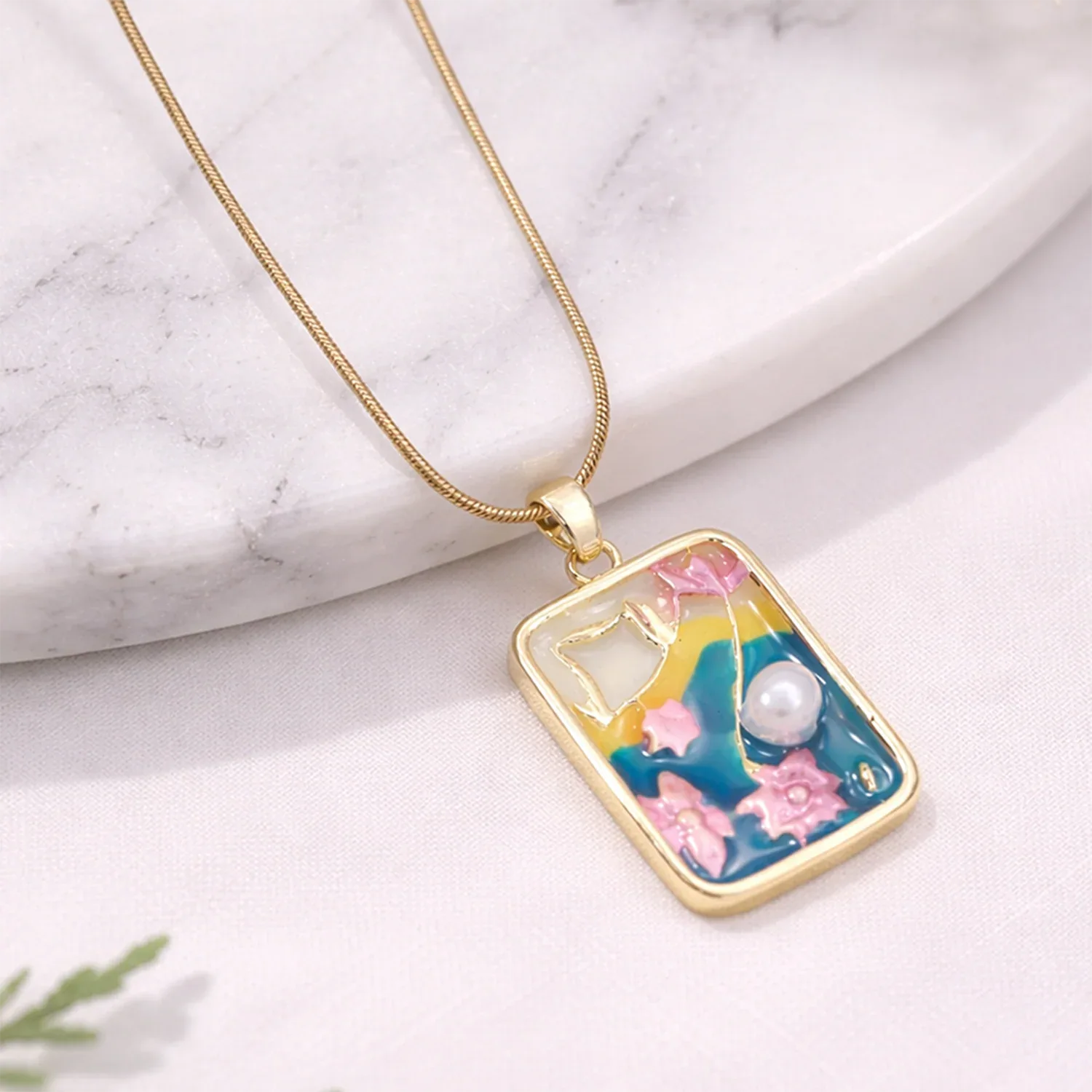 Necklace with a colorful pendant featuring flowers and a pearl on a marble surface.