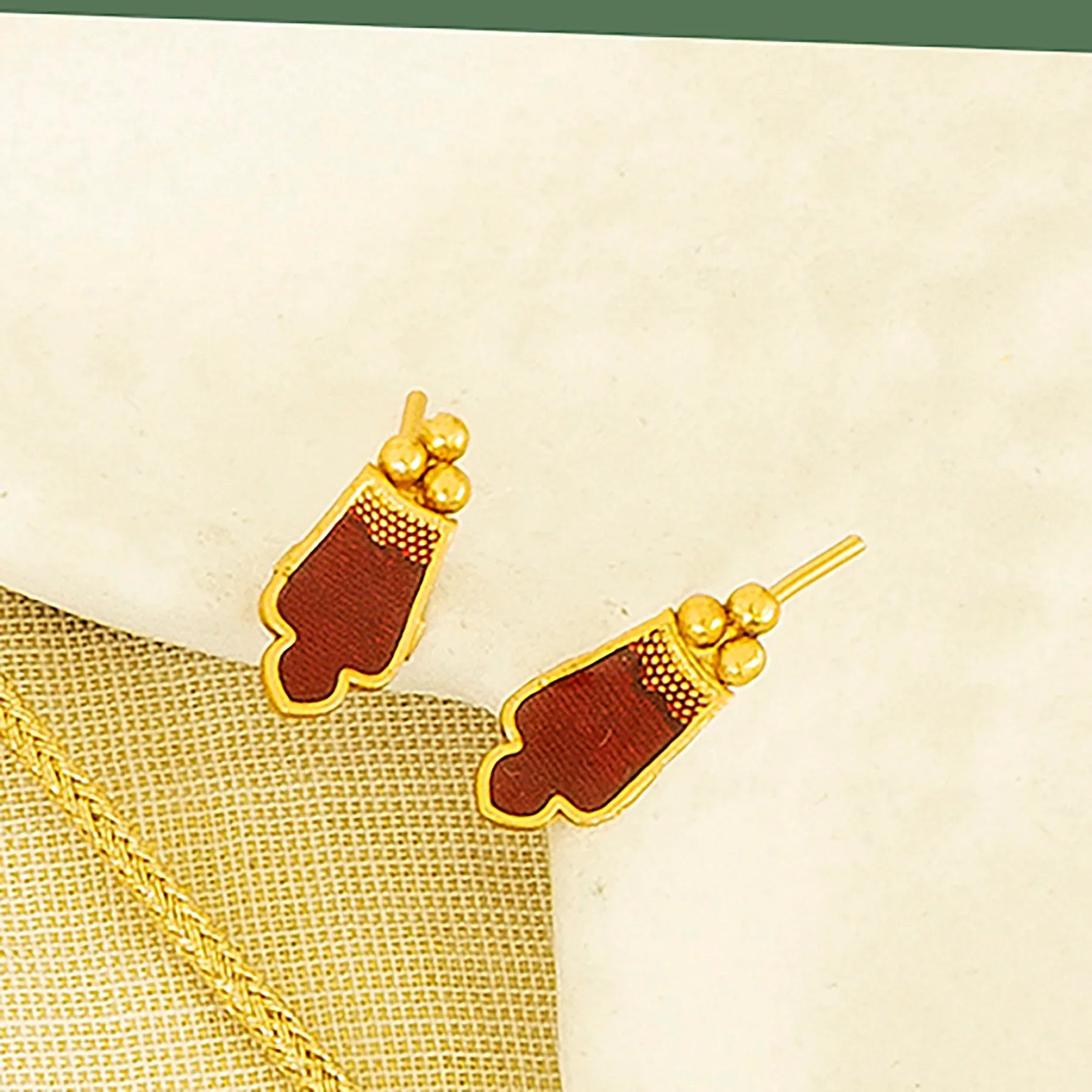 Gold earrings with brown heart-shaped pendants on a beige fabric background