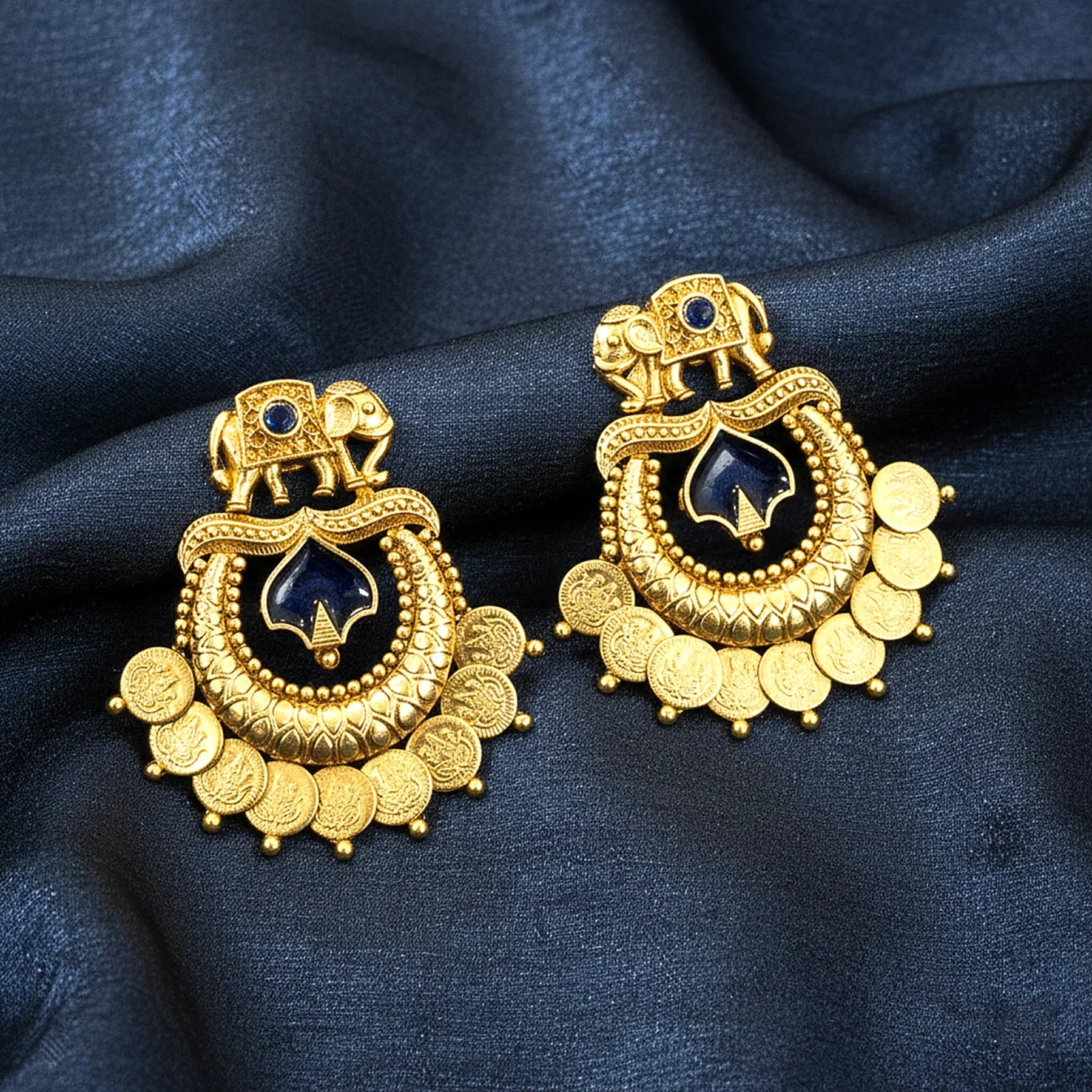 Gold earrings with blue stones on a dark blue fabric background