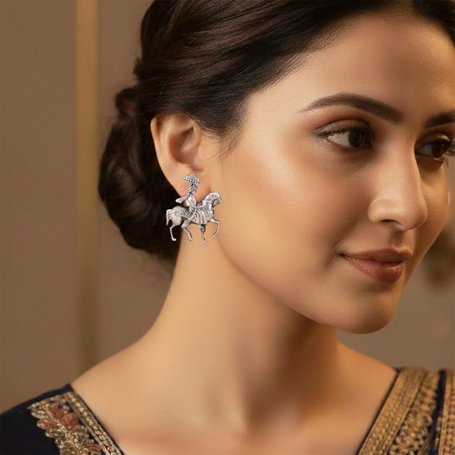 Woman wearing a silver earring with a horse design on a neutral background