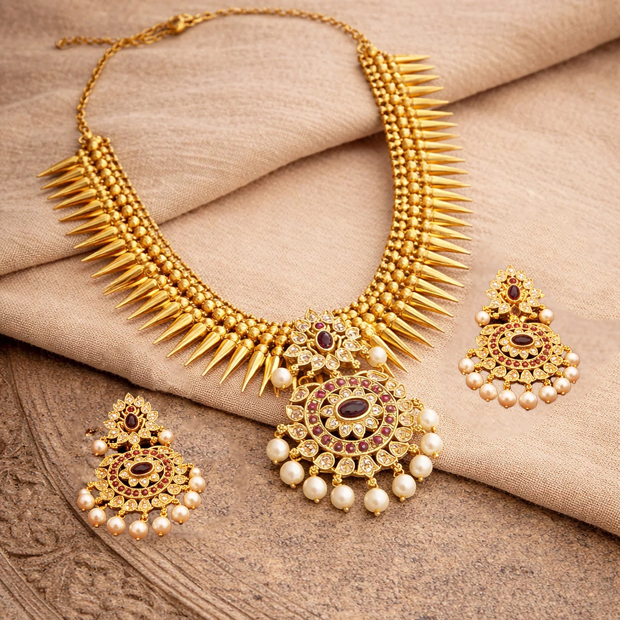 Gold necklace and earrings set on a beige fabric background
