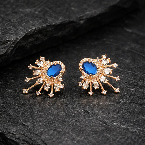 Pair of gold earrings with blue gemstones on a dark stone surface