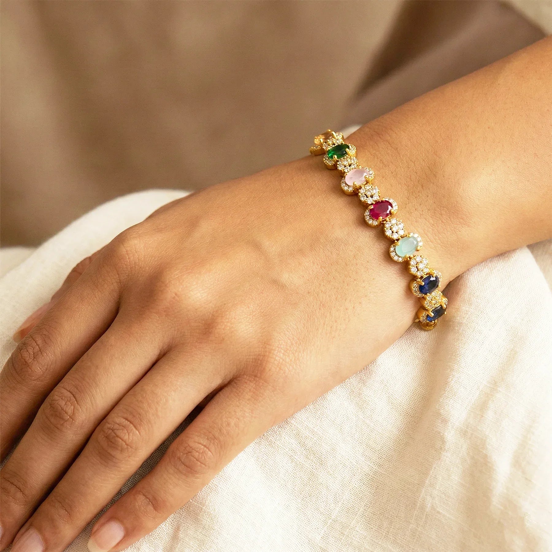 Gold bracelet with colorful gemstones on a wrist against a neutral background
