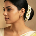 Woman with floral hairpiece and gold earrings against a beige background