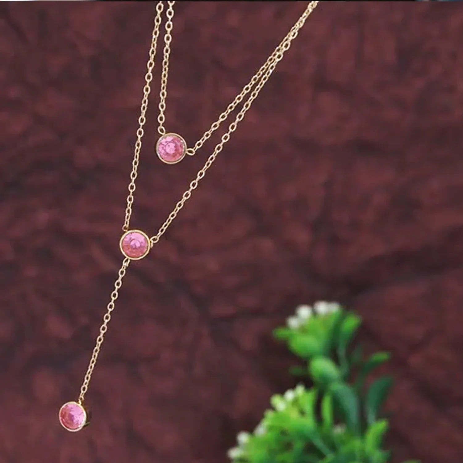 Gold necklace with pink gemstones on a textured brown background