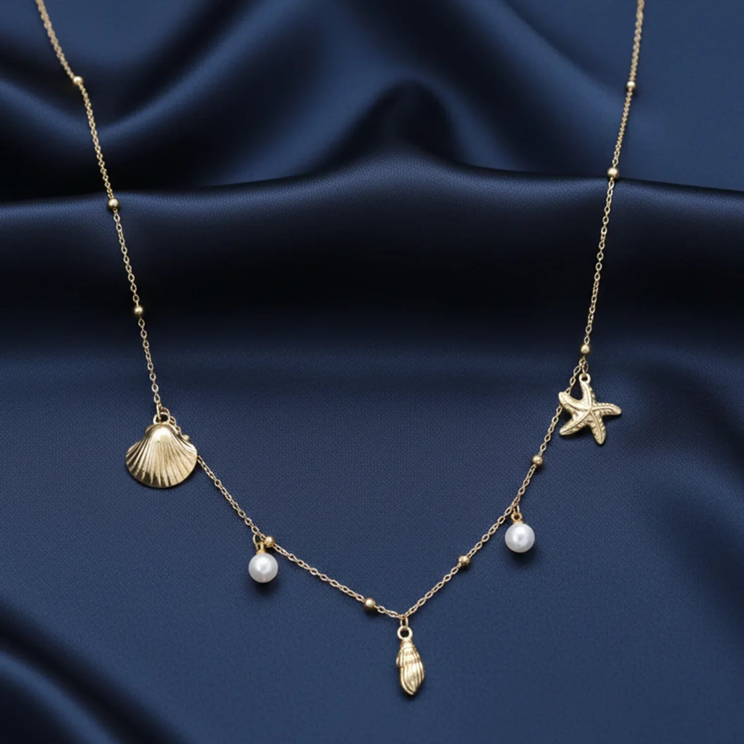 Necklace with shell, starfish, and pearl pendants on a dark blue fabric background