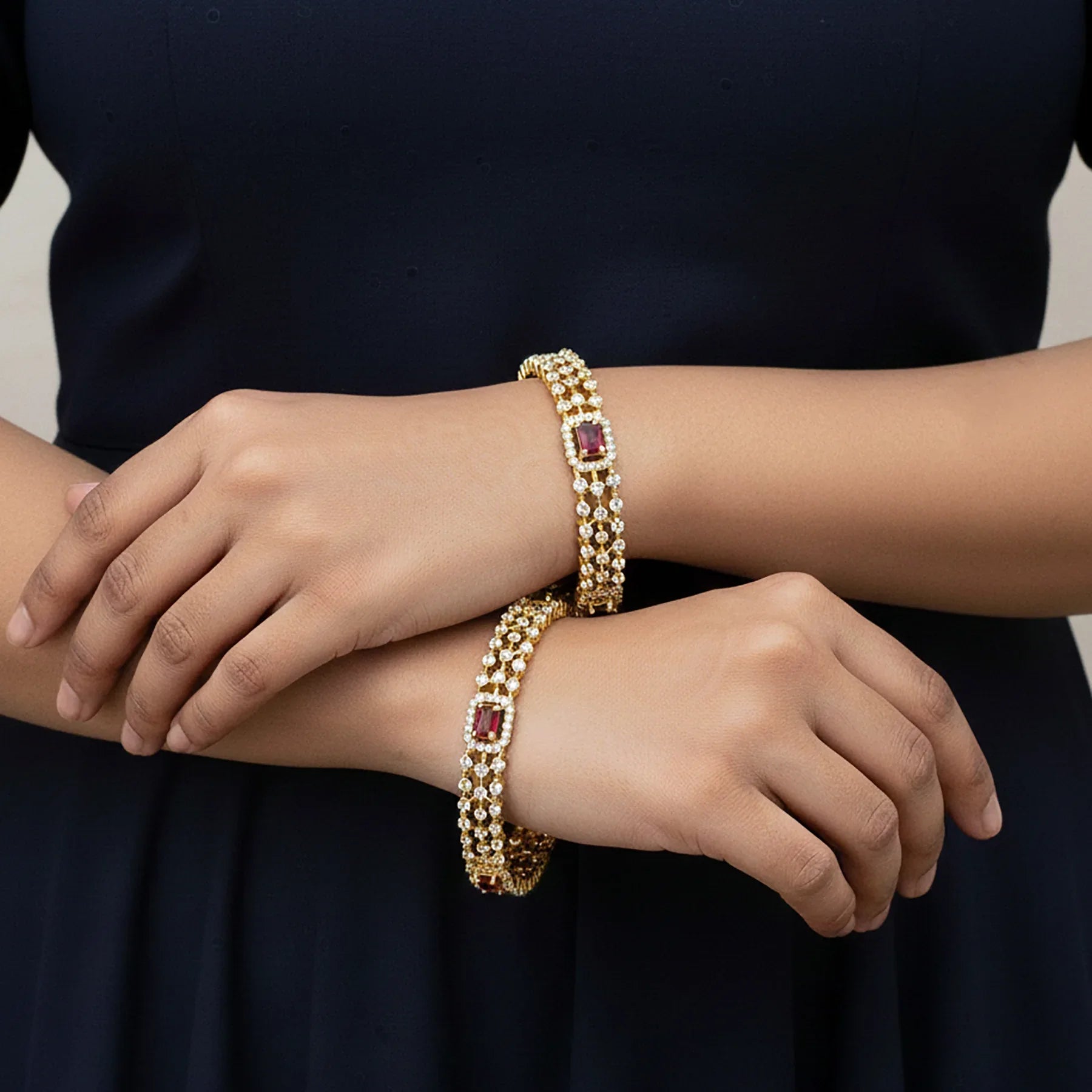 Gold bracelets with red gemstones on a person's wrist against a dark background