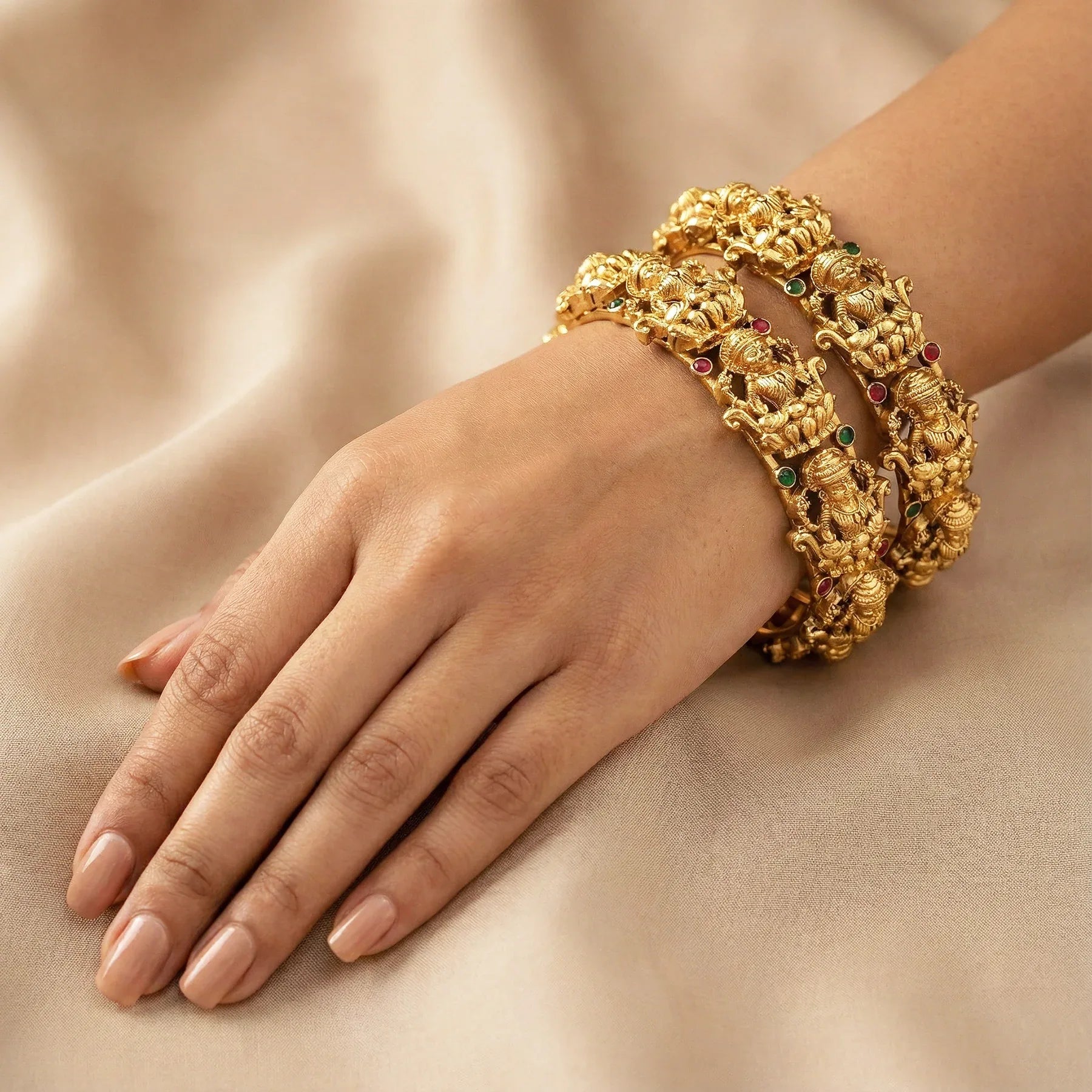 Gold bracelet with gemstones on a hand against a beige fabric background