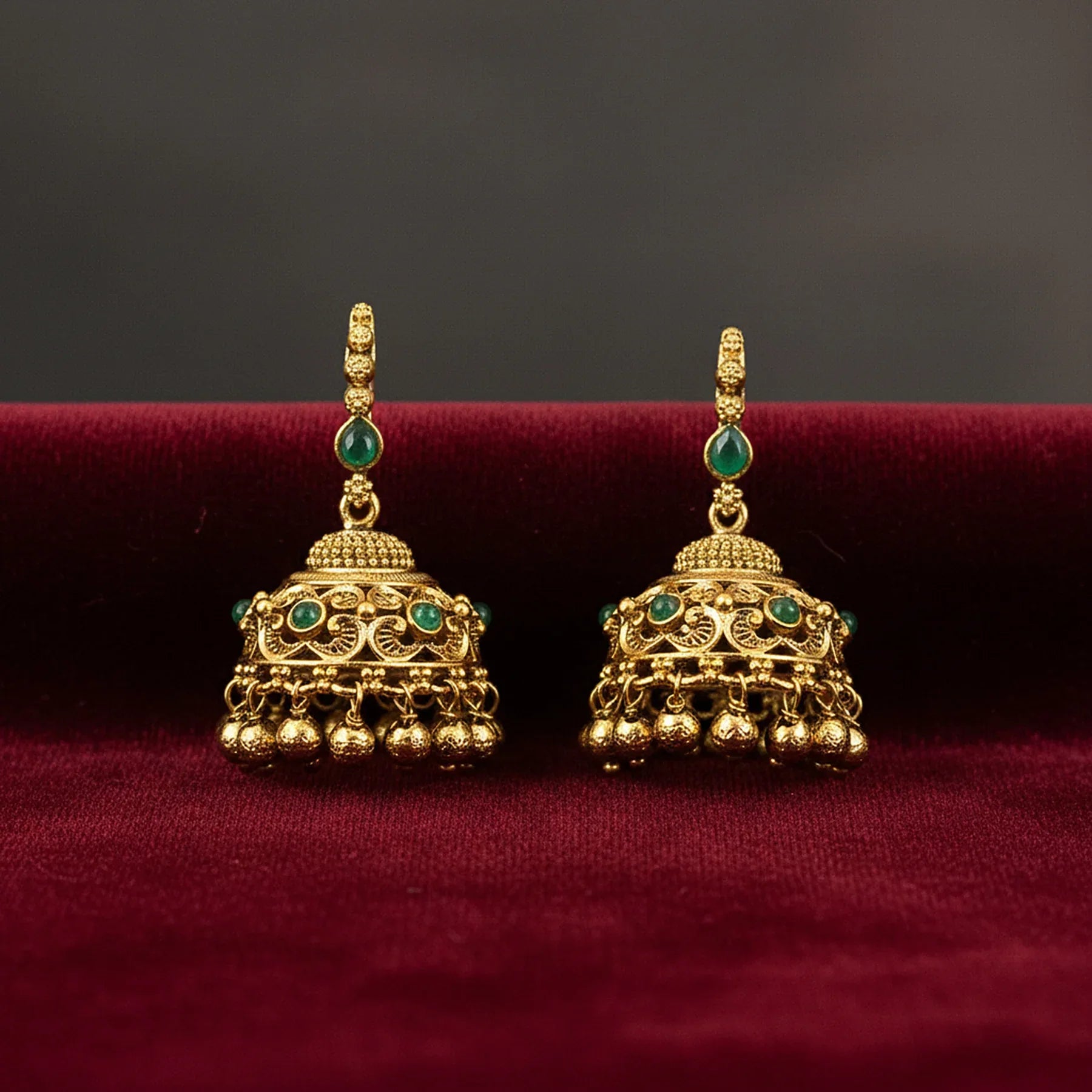 Gold earrings with green gemstones on a red surface