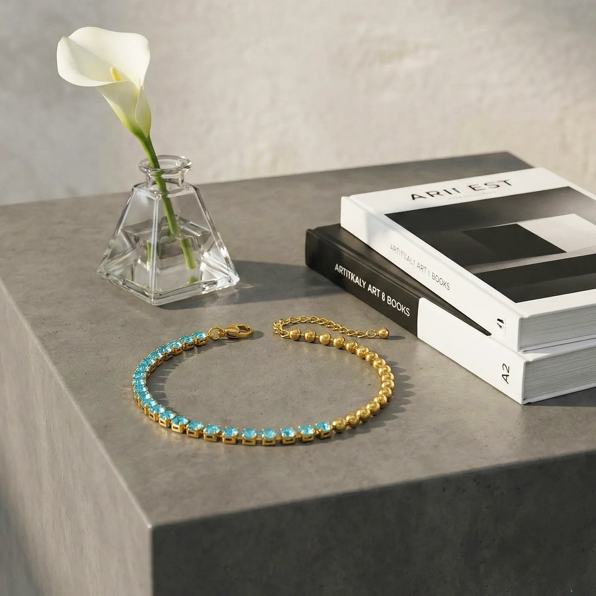 Gold bracelet with blue stones on a gray surface with books and a vase in the background