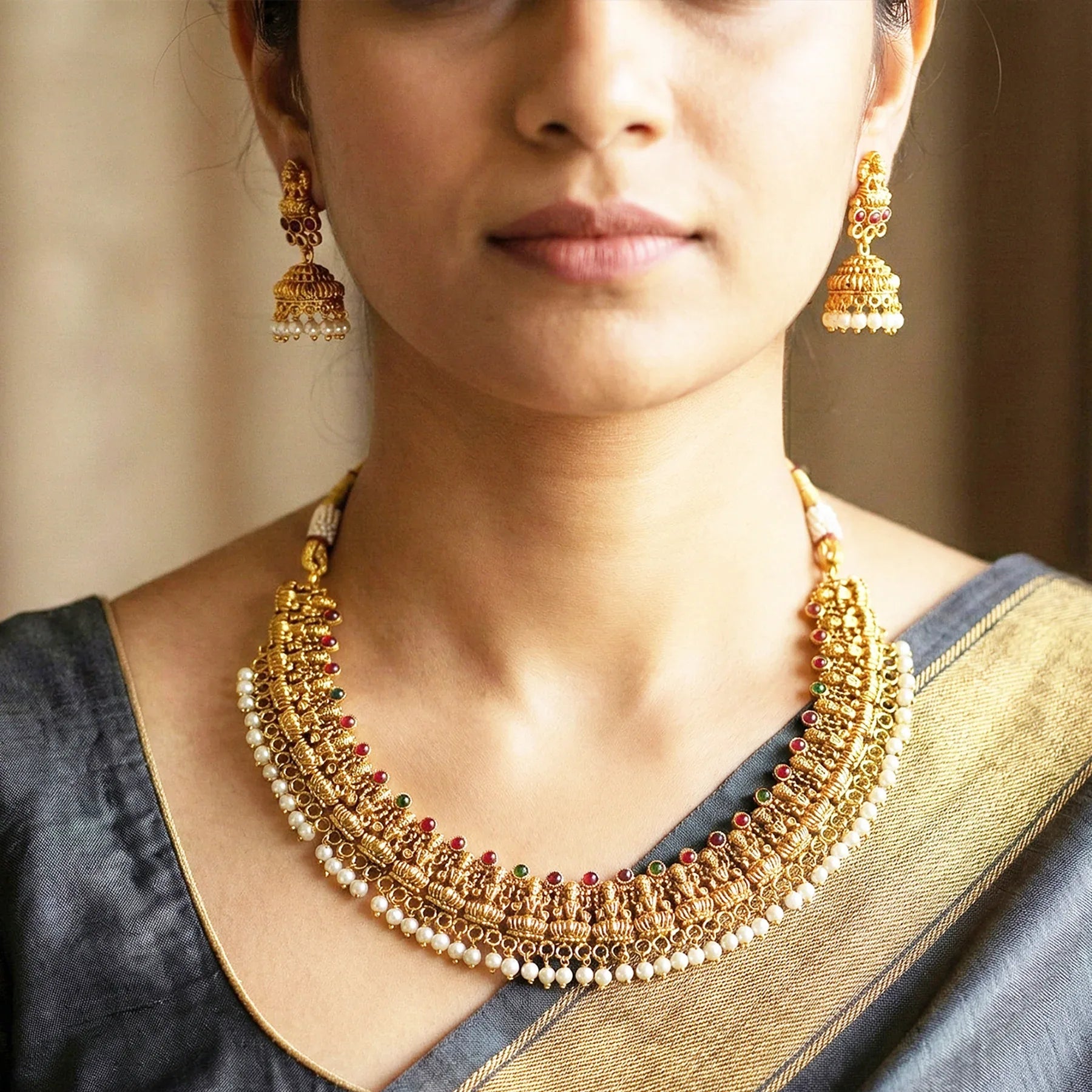 Woman wearing a gold necklace and earrings with a neutral background
