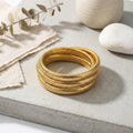 Set of gold bangles on a neutral background with stones and leaves