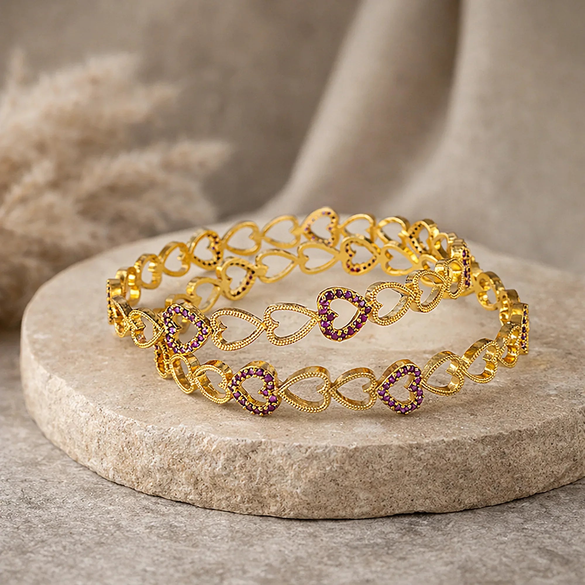 Gold bracelet with heart-shaped purple stones on a stone surface
