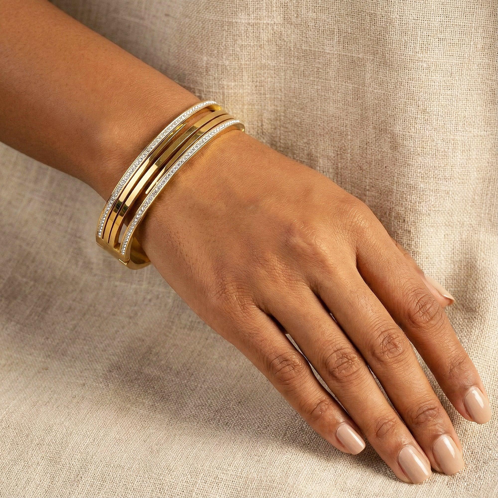 Hand wearing a gold bracelet on a beige fabric background