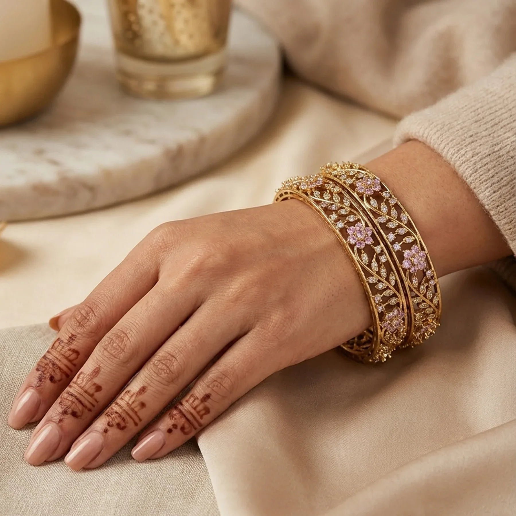Hand wearing gold bangles with intricate designs on a neutral background