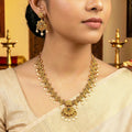 Woman wearing a gold necklace and earrings with a blurred background