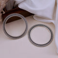 Two silver bangles on a light surface with a white fabric background