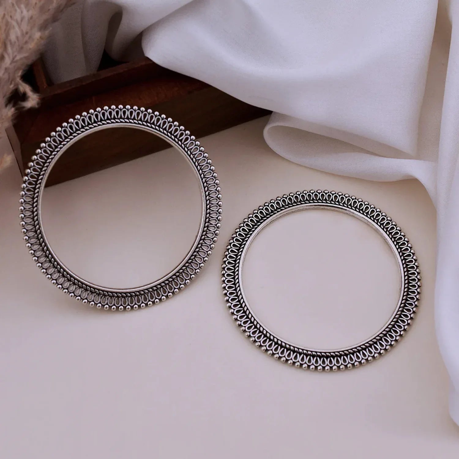 Two silver bangles on a light surface with a white fabric background