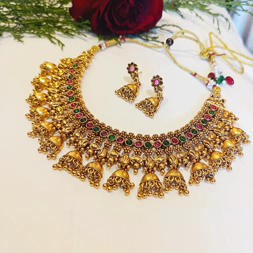 Gold necklace and earrings with gemstones on a white surface with a red rose and green leaves.