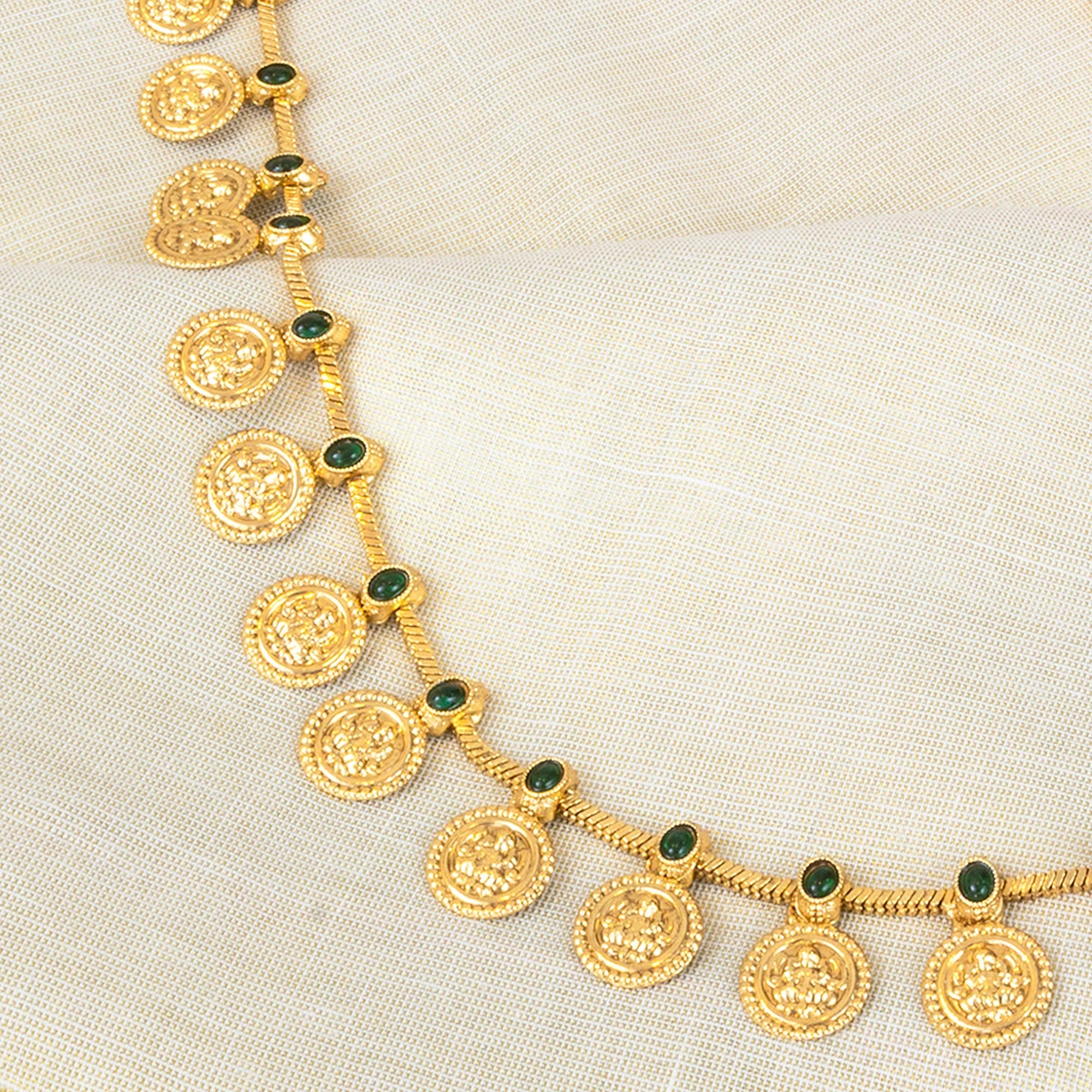 Gold necklace with green gemstones on a beige fabric background