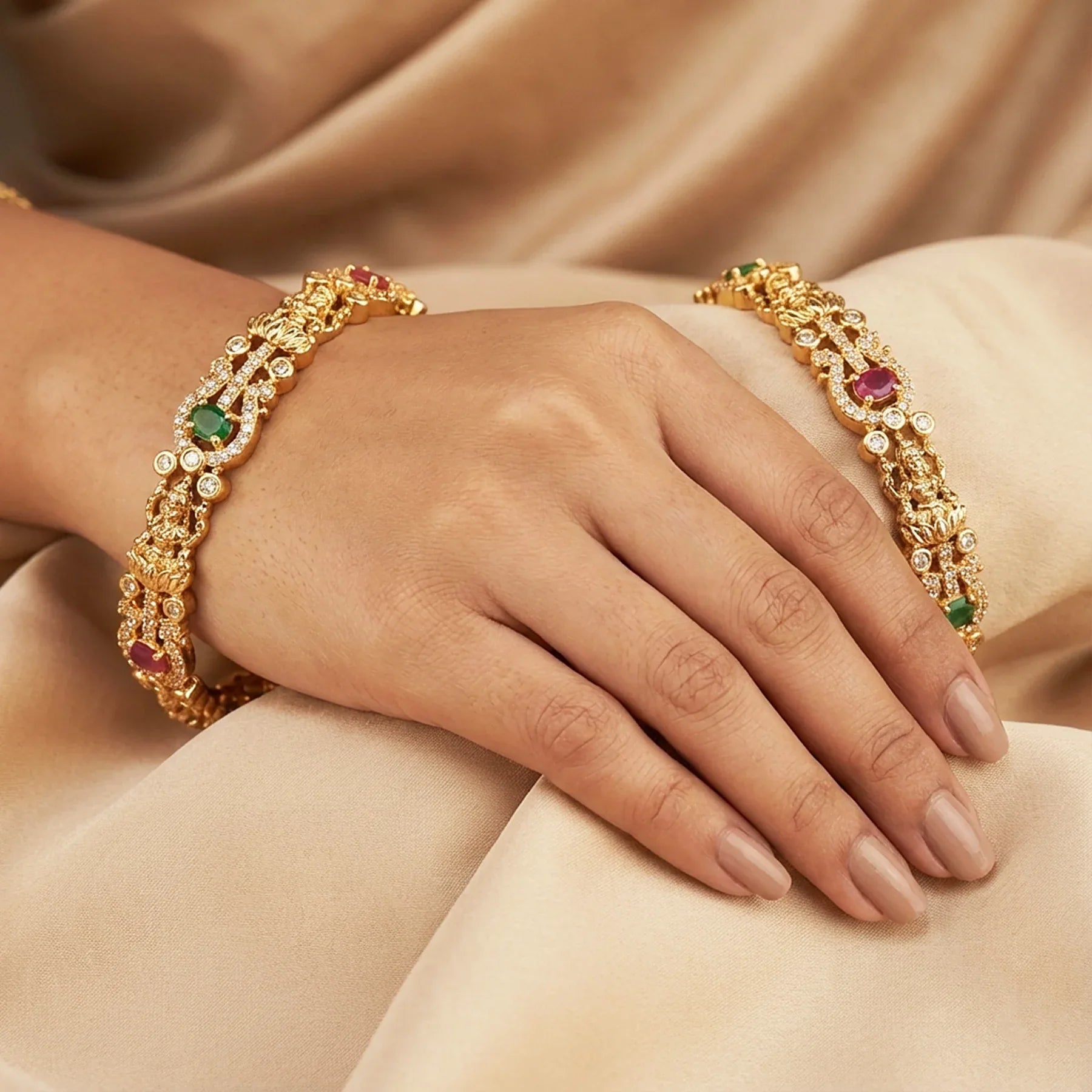 Gold bracelets with gemstones on a hand against a beige fabric background