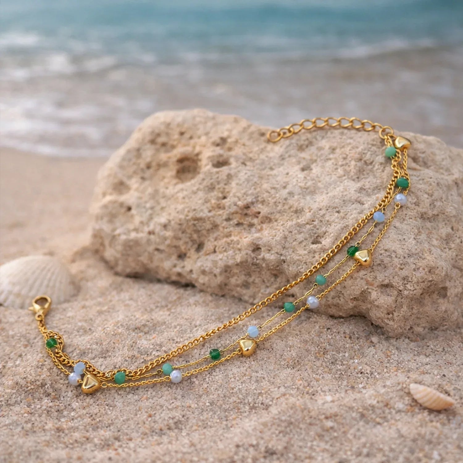 Gold necklace with green and blue beads on a rock by the beach