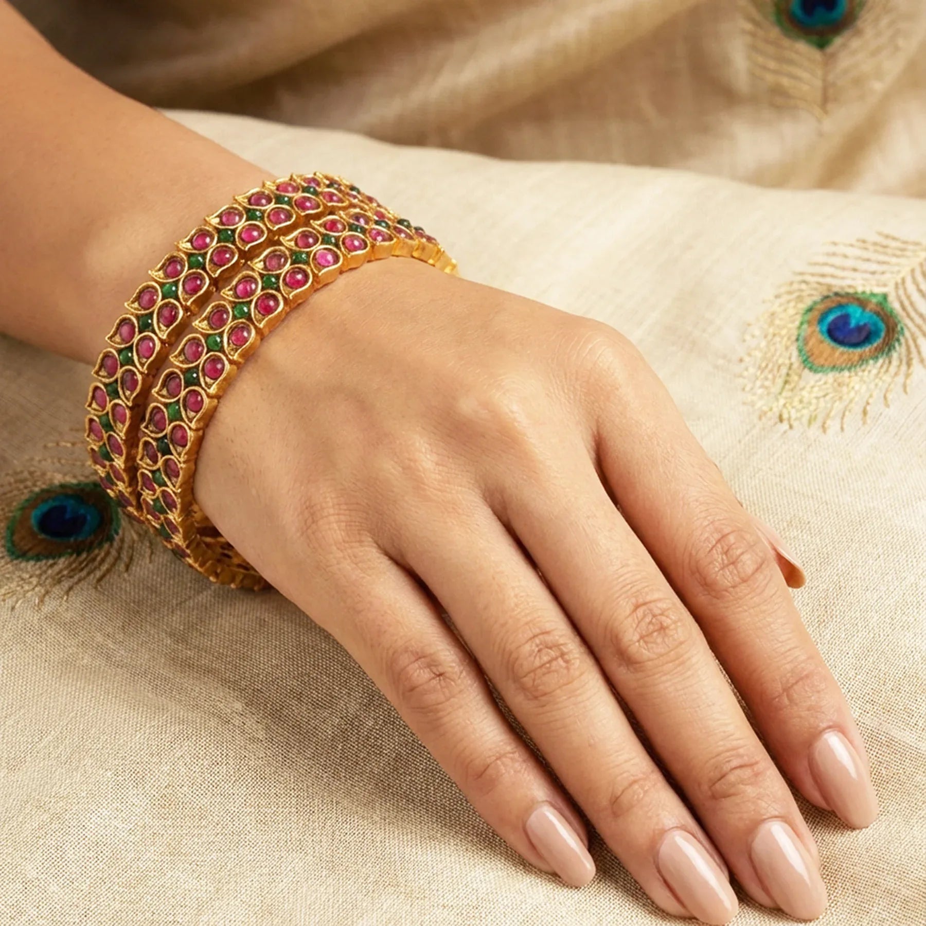 Hand wearing a gold bracelet with gemstones on a textured fabric background