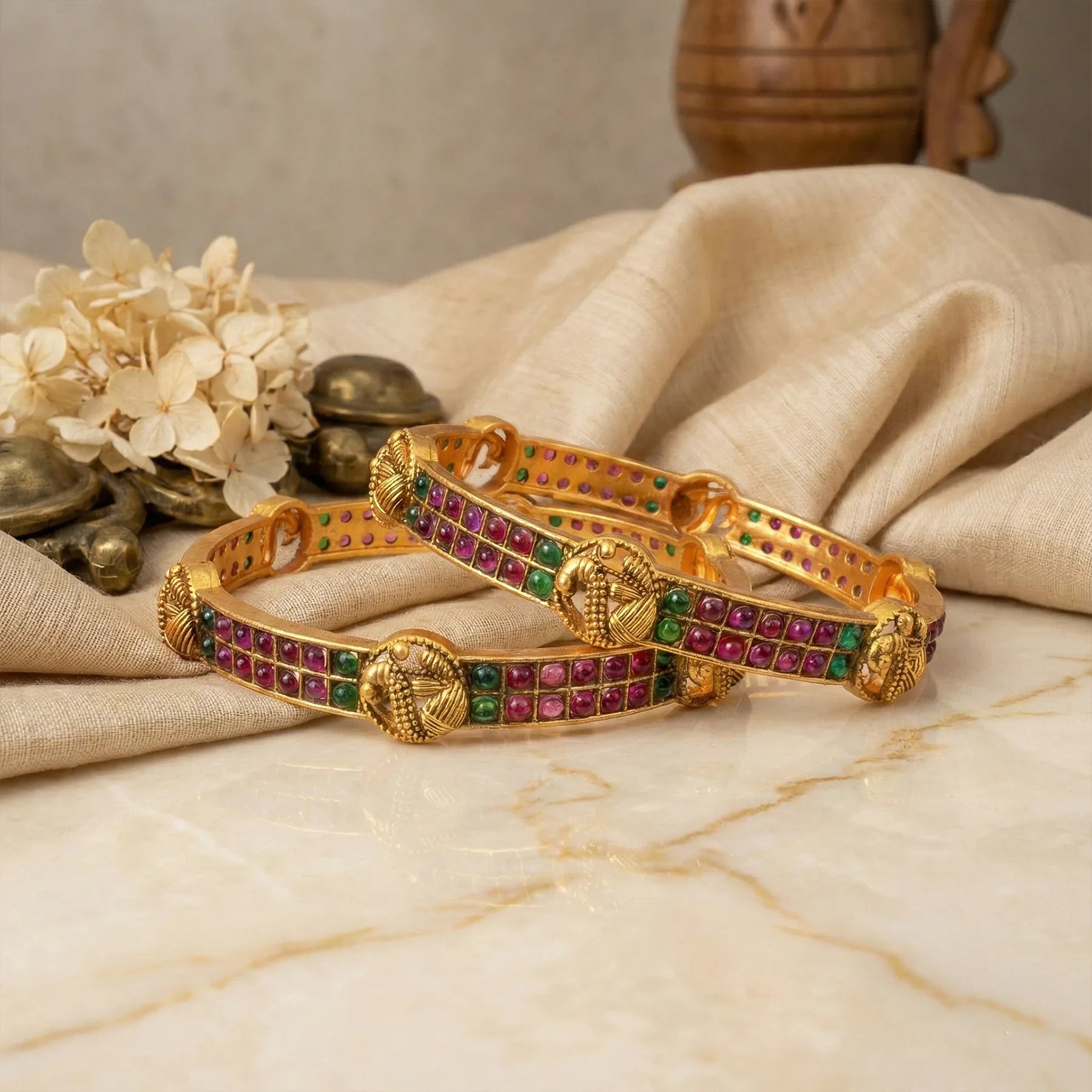 Gold bracelet with colorful stones on a marble surface with flowers and coins in the background