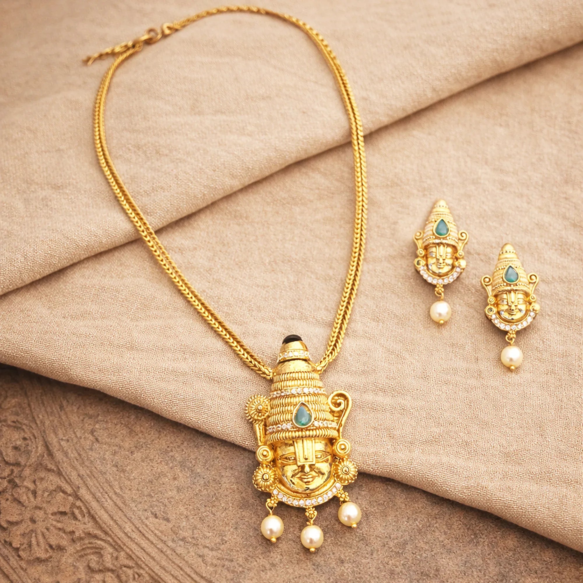 Gold necklace and earrings on a beige fabric background