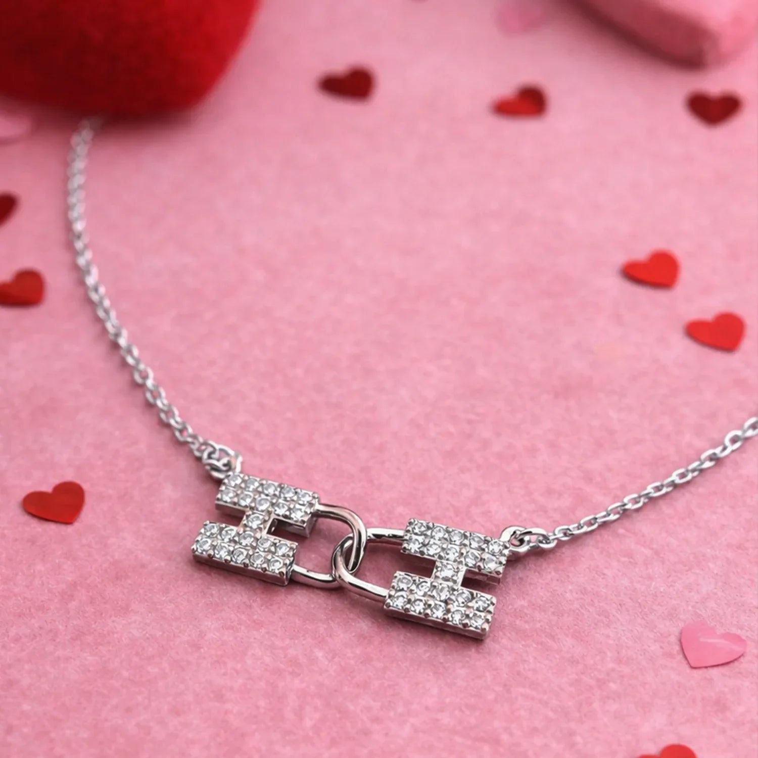 Silver necklace with a clasp on a pink background with heart shapes