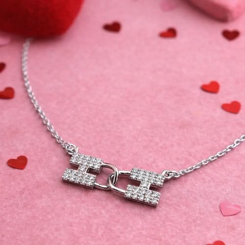 Silver necklace with a clasp on a pink background with heart shapes