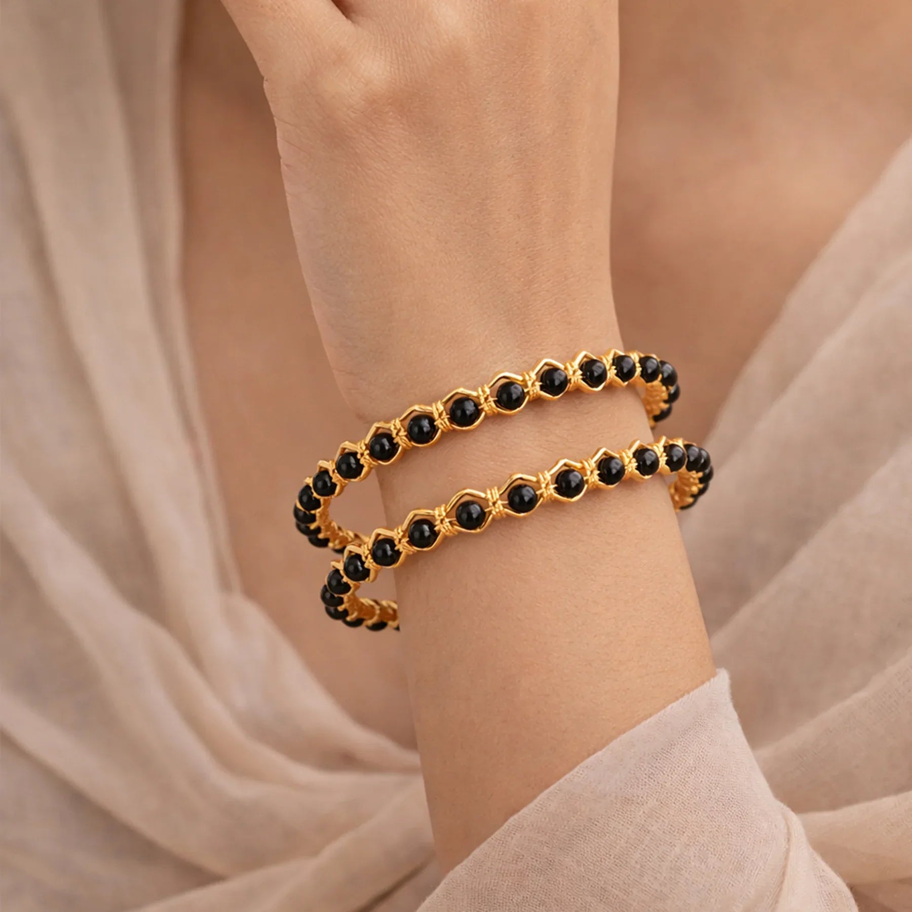 Gold and black beaded bracelet on a wrist with a soft beige background