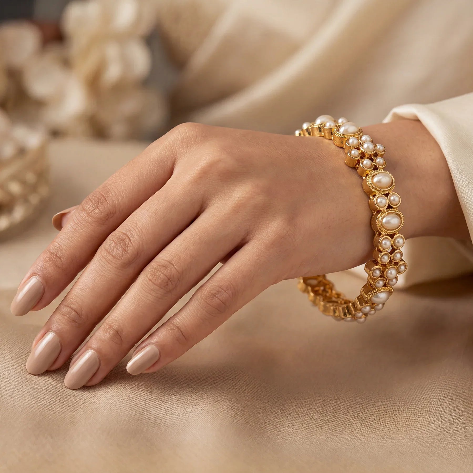 Hand wearing a gold and pearl bracelet on a neutral background