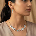 Close-up of a woman wearing a necklace and earrings with a neutral background